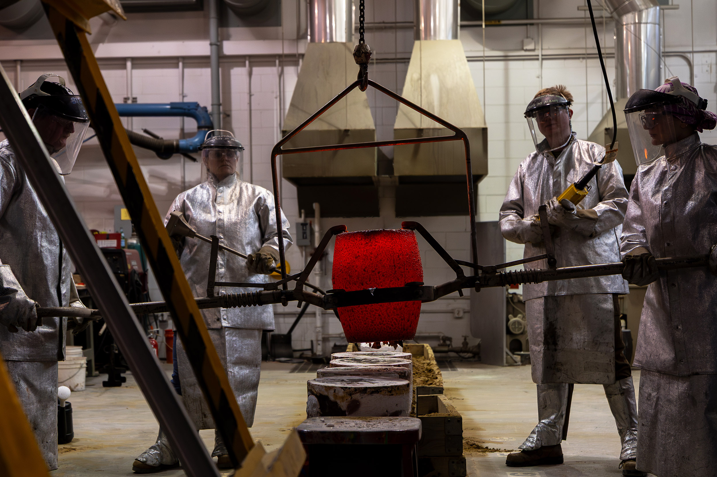 Four people carefully operate a crucible during a bronze metal pour at the Boor sculpture studio at UAlbany.