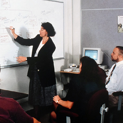 a woman teaches at a whiteboard as older students look on.