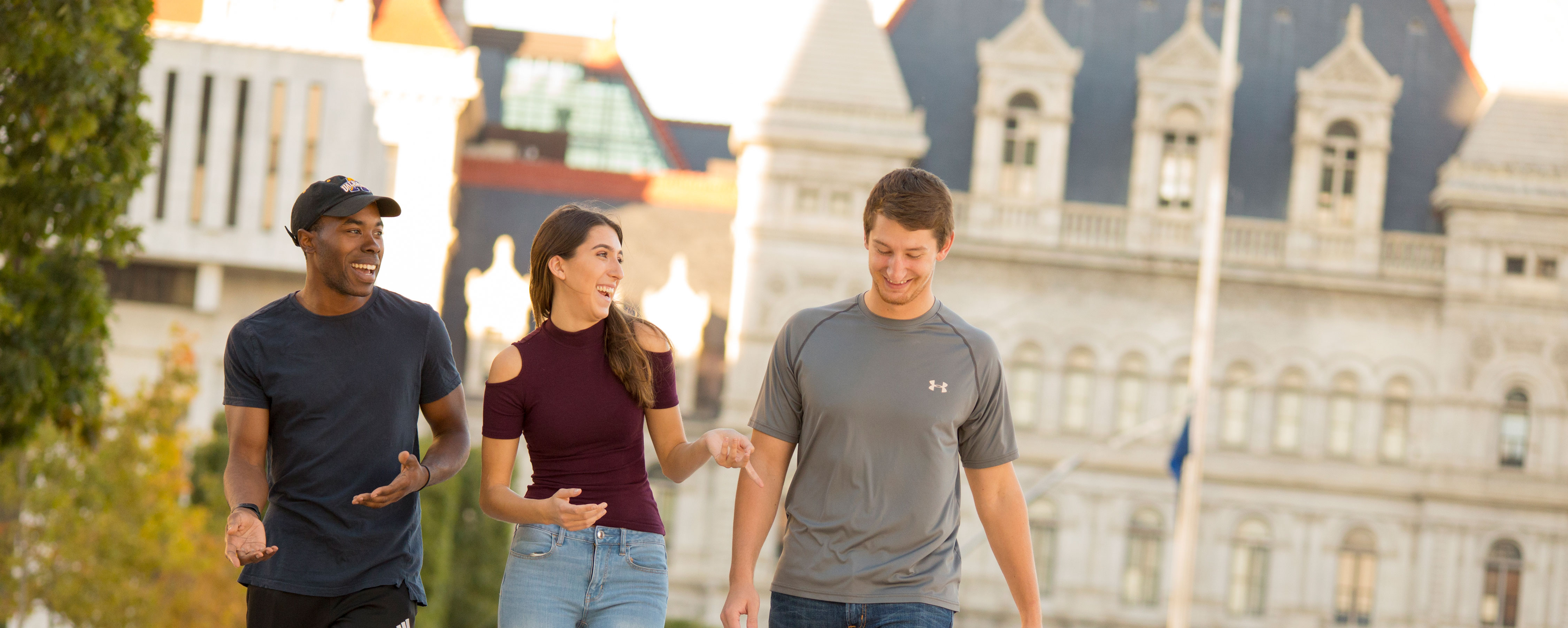 Three students smile and laugh as they walk along the Empire State Plaza near the Capitol.