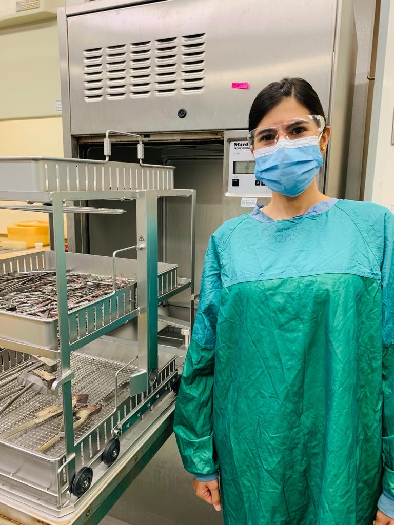 Maria Isabel is wearing protective gear and stands next to lab equipment at the state health department.