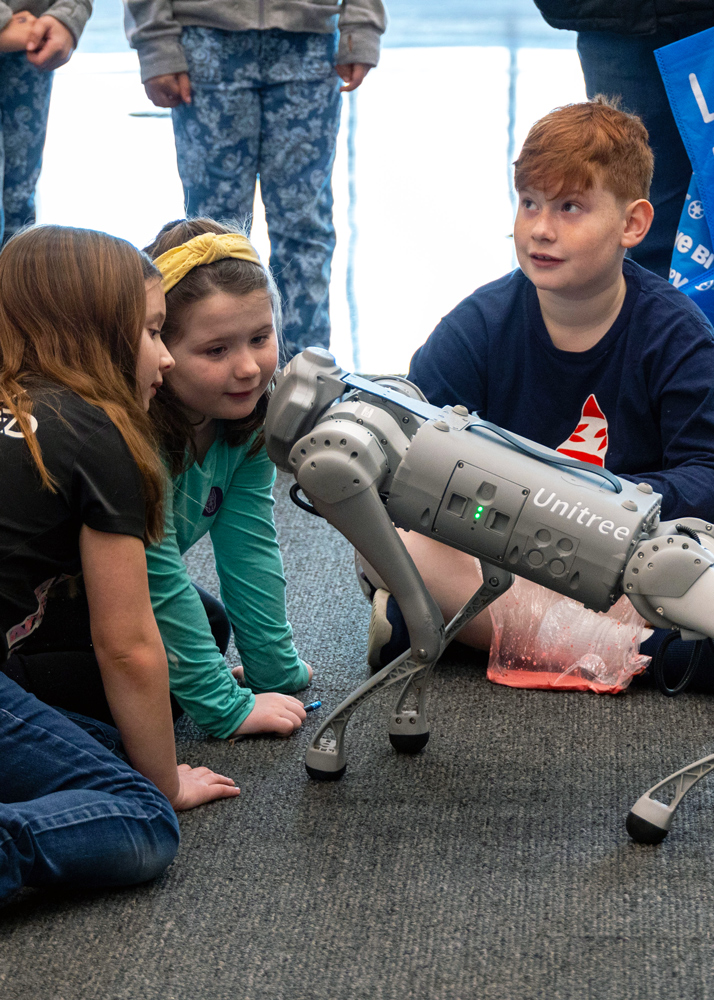 Three children interacting with a robot dog at UAlbany STEM and Nanotechnology Family Day.