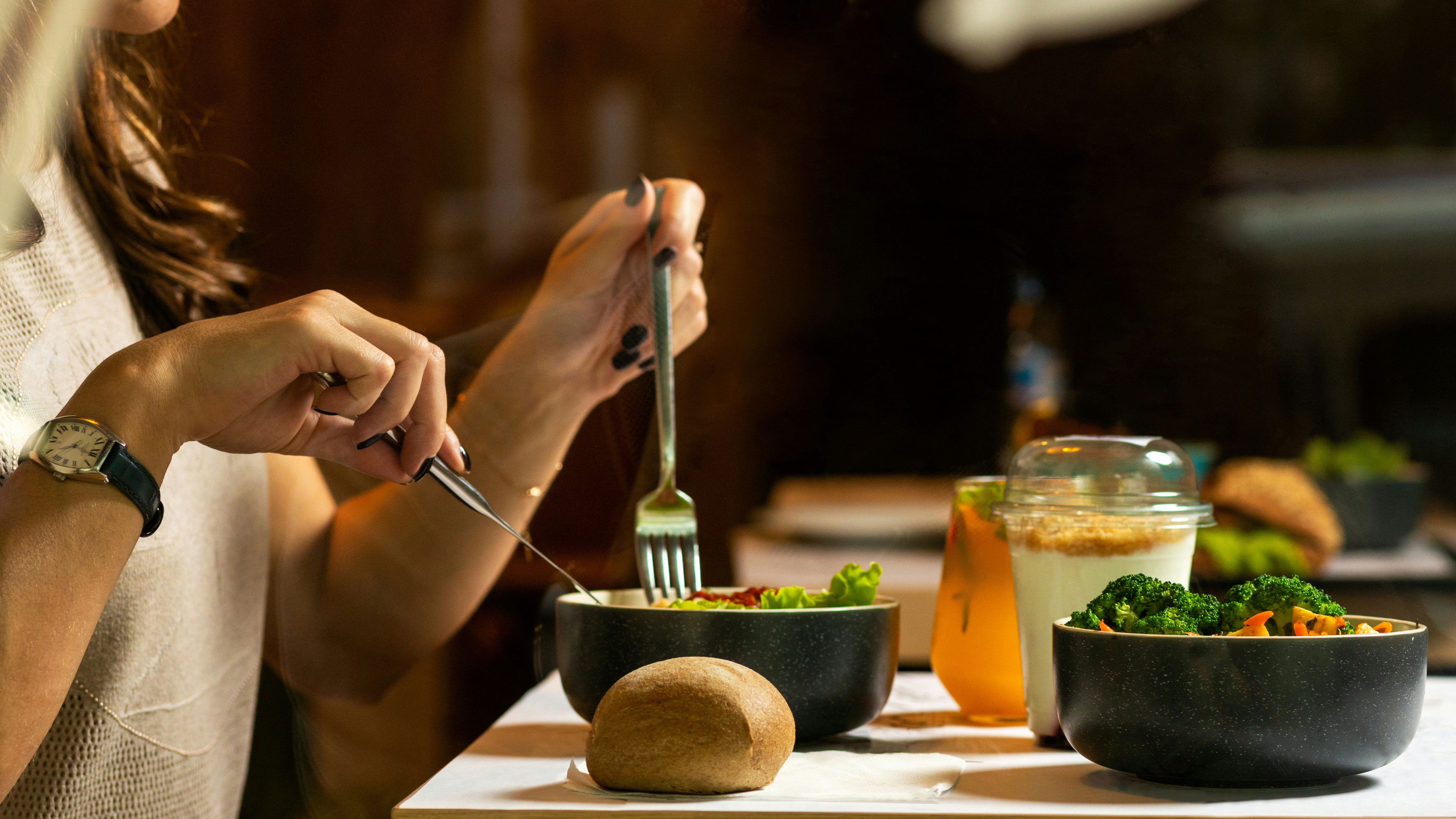 A person seated at a table, savoring a bowl of food with a fork and knife in hand.