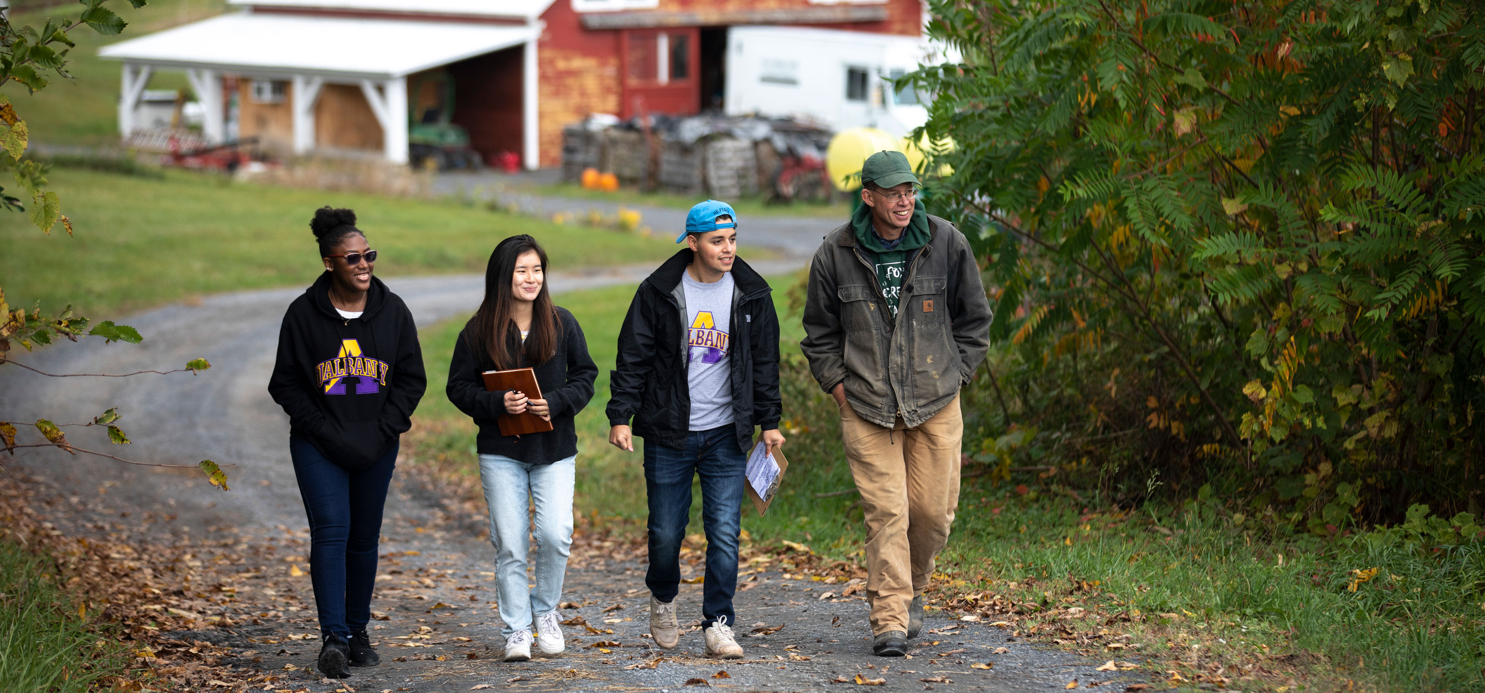 Three students and a farmer walk up a hilly access road on a local farm during a service learning project.