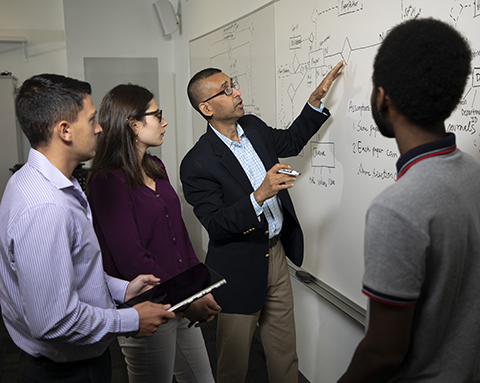 Digital Forensics program director Sanjay Goel and students look at a white board in the digital forensics lab at UAlbany.