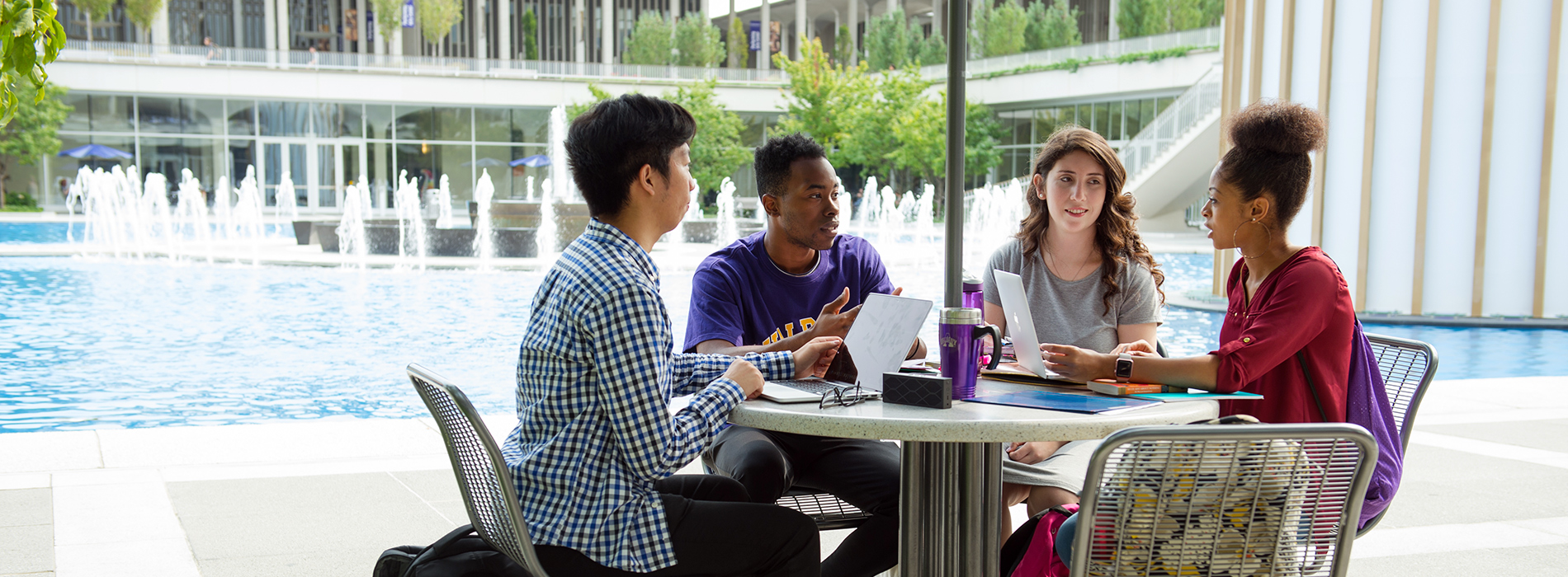 Four students having a discussion at a table next to the UAlbany main fountain.
