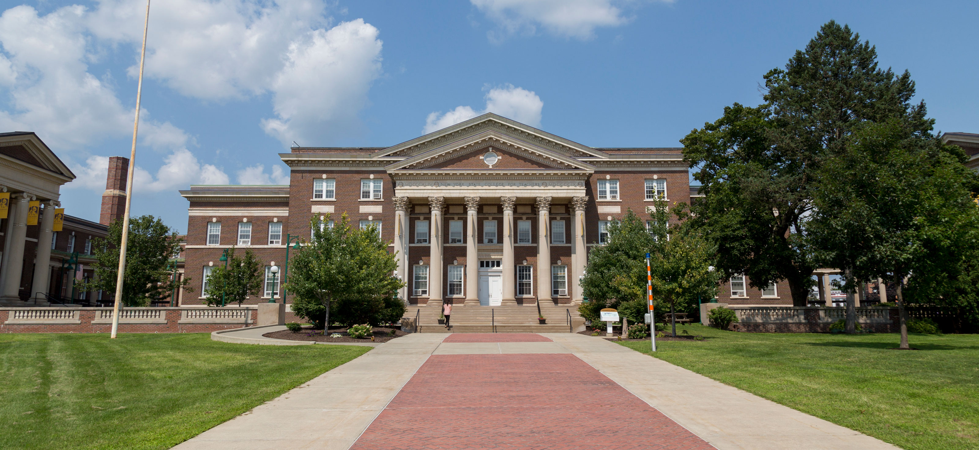 A brick Downtown Campus building with six tall columns and a brick walkway on a sunny day.