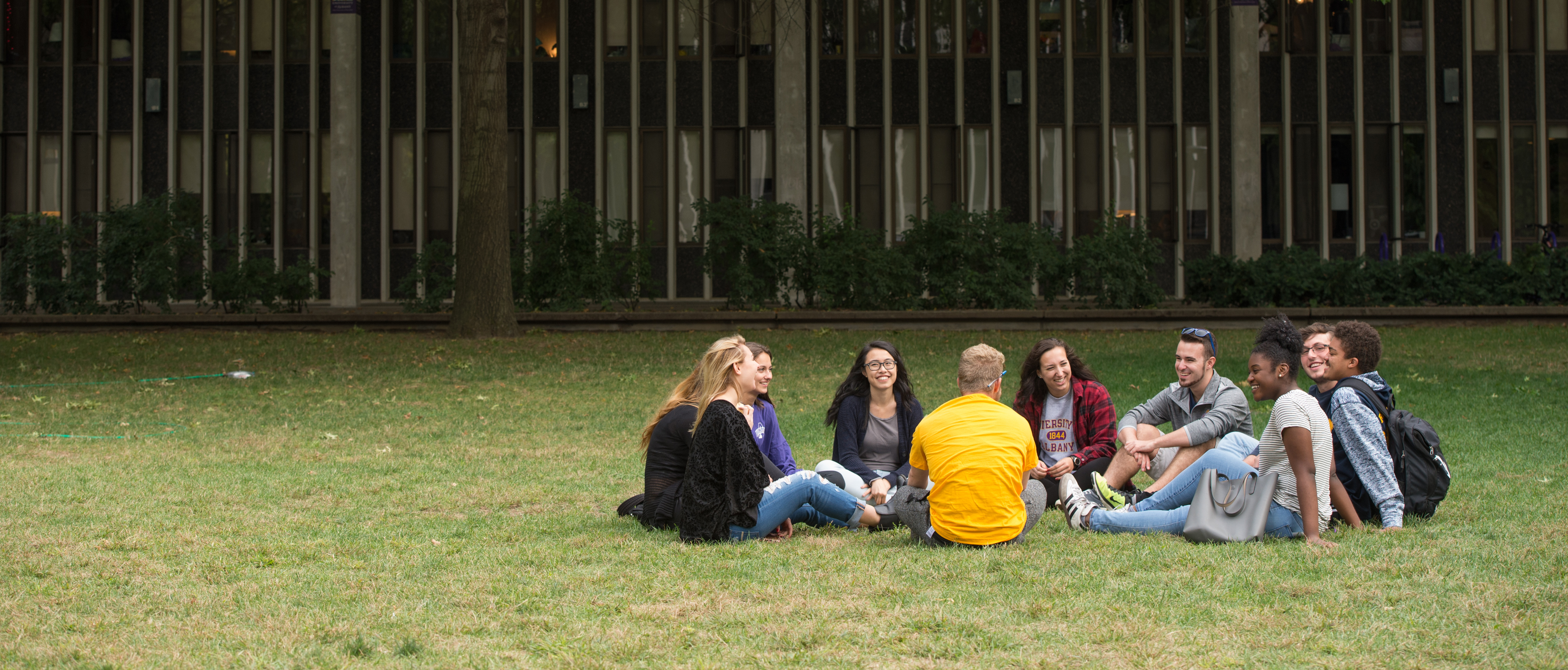 10 students sit in a circle on the grass outside a residence hall