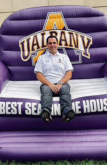 Stefanos Marcopoulos sits in the UAlbany "Best Seat in the House" inflatable chair at Casey Stadium.