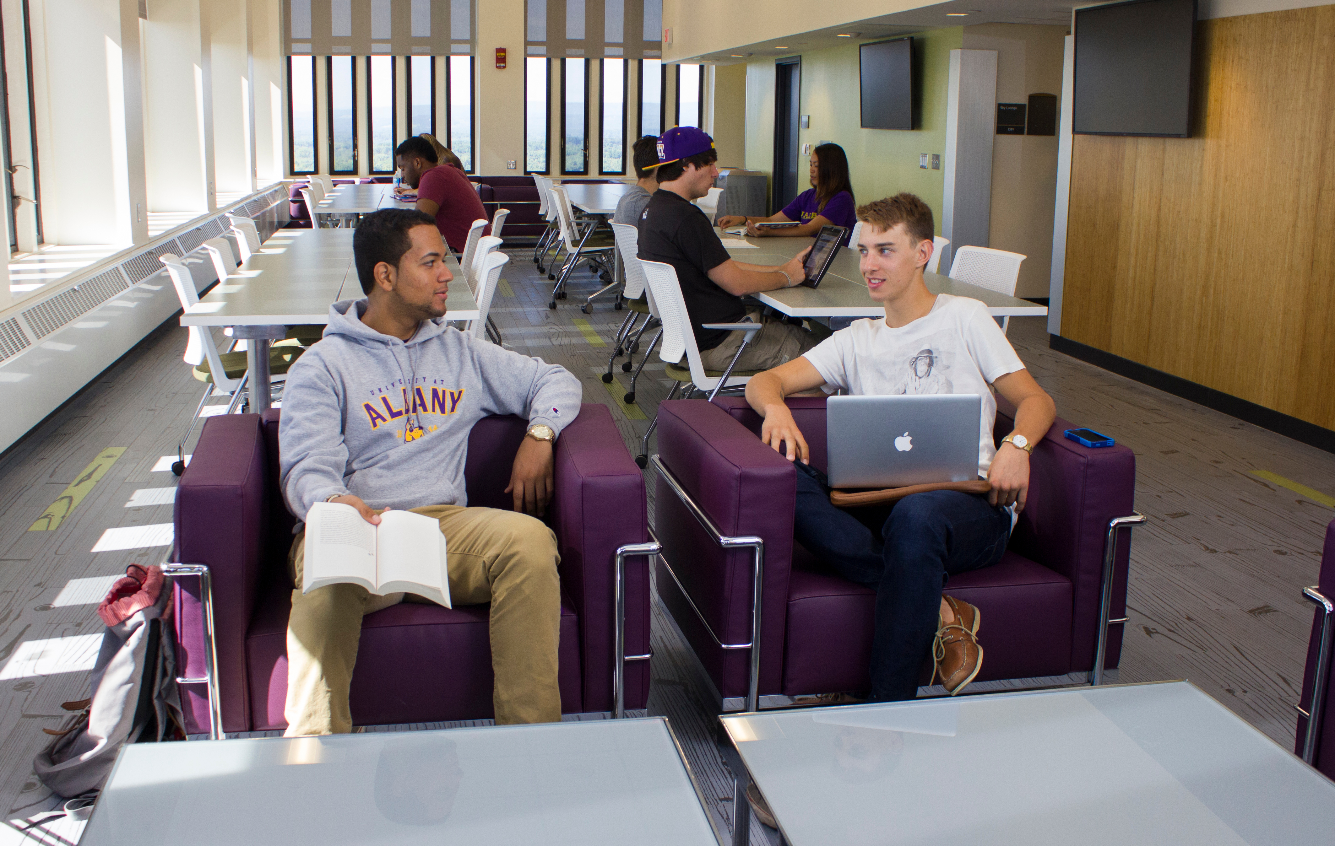 Seven students work inside the Indigenous Quad Penthouse's study lounge, which has purple chairs, long tables and large windows
