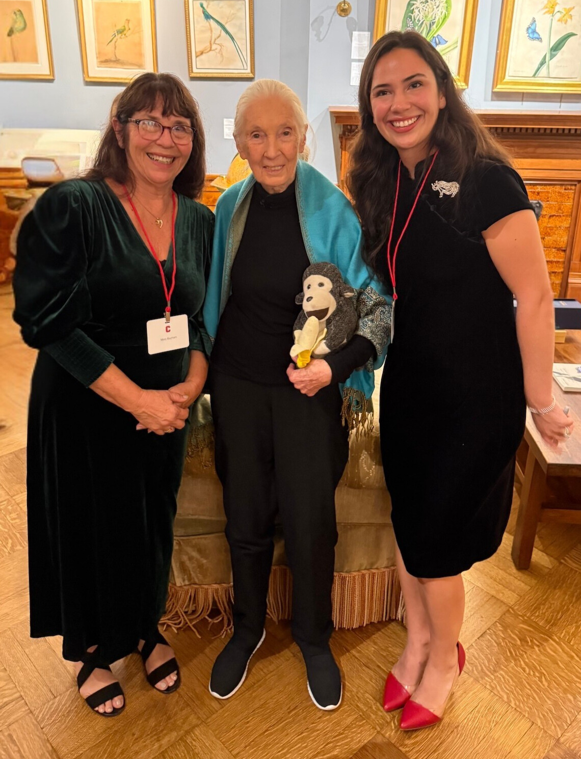 Three women smile and stand together with primatologist Jane Goodall in the middle. 