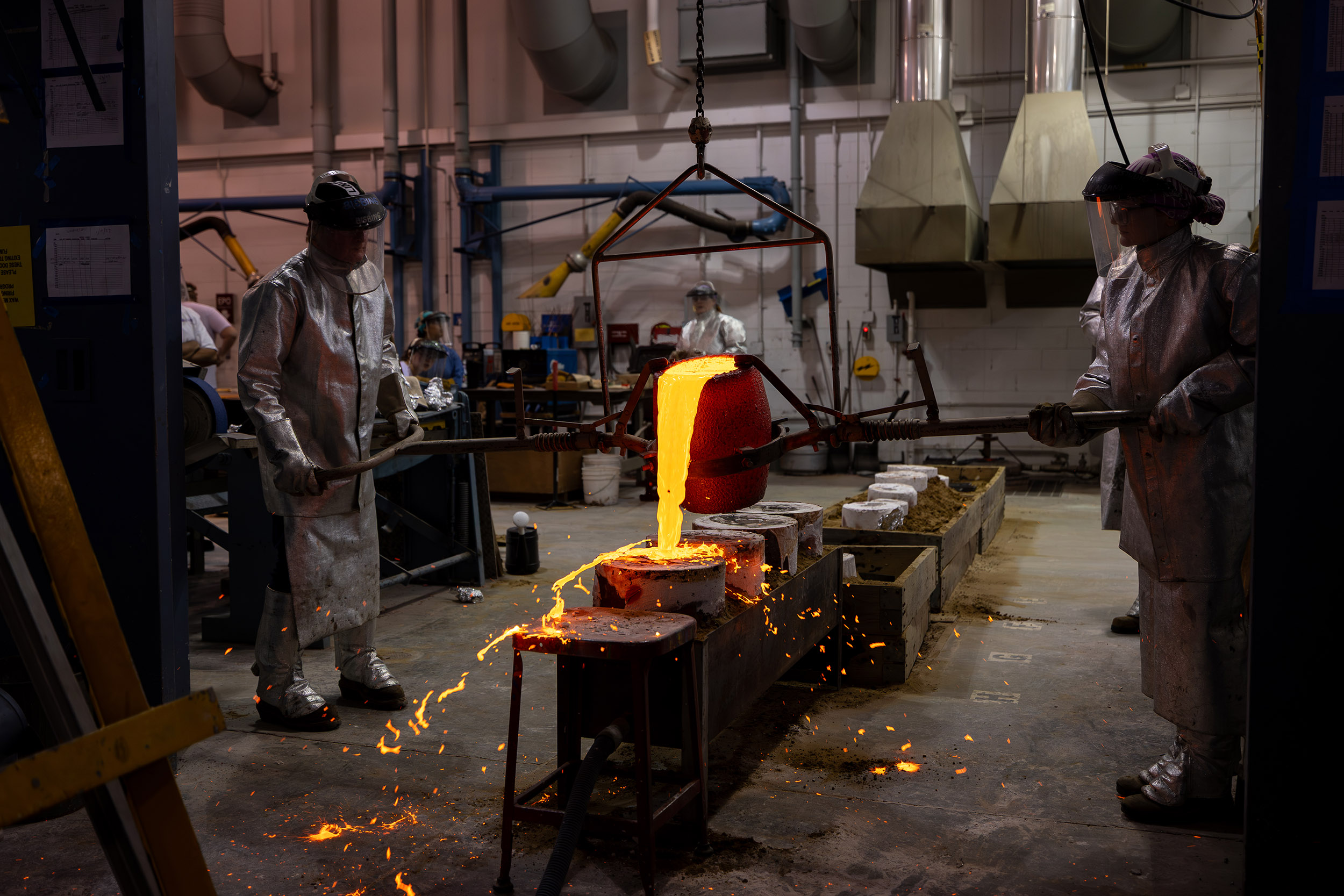 Two technicians wearing protective gear pour molten bronze into sculpture casts as the Boor Sculpture Studio at UAlbany.