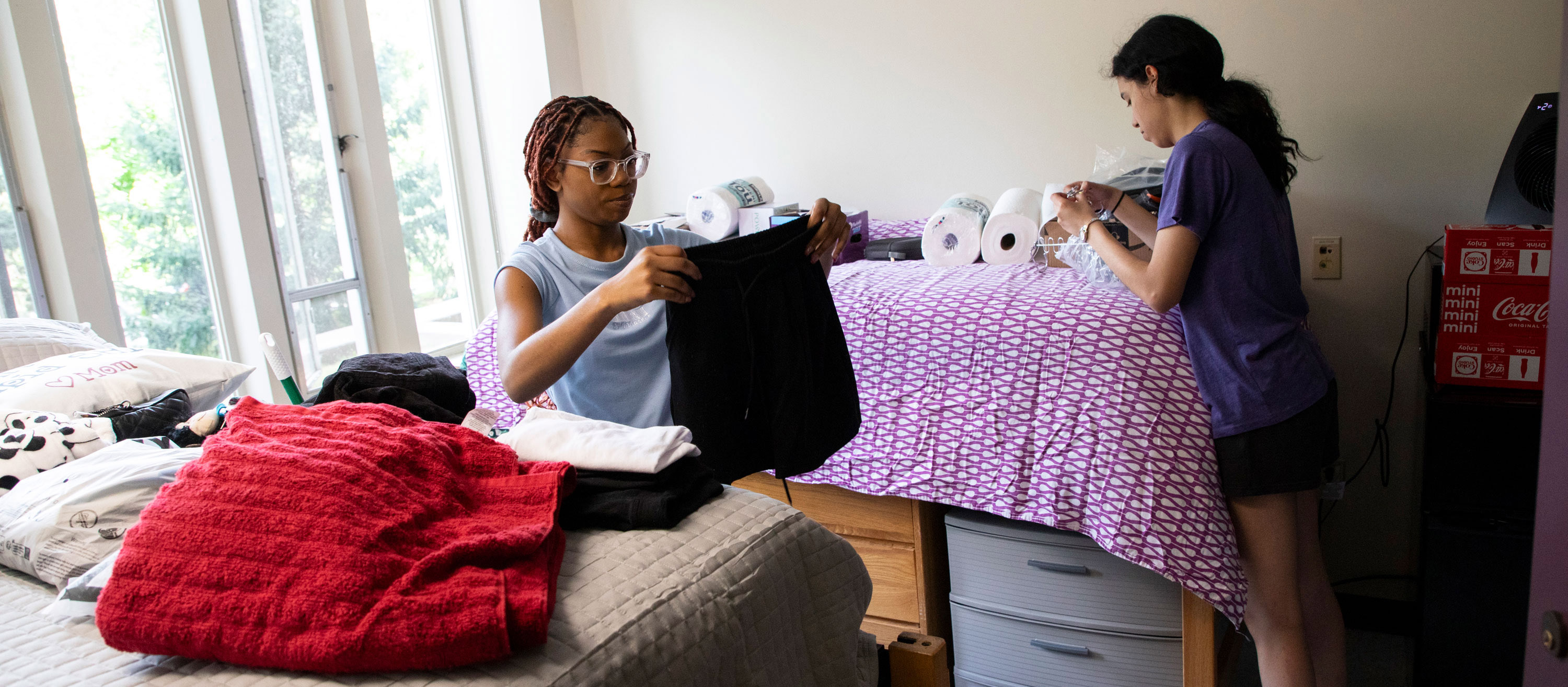 Two students unpack clothing and other belongings inside their two-person residential hall bedroom.