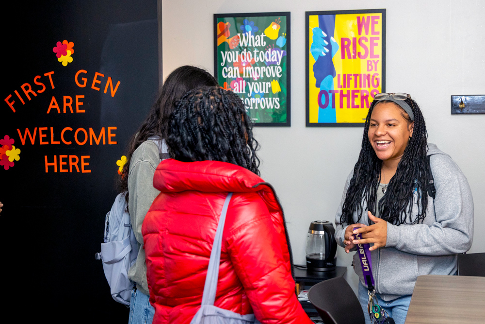 Three people having a conversation in an office with inspirational posters.