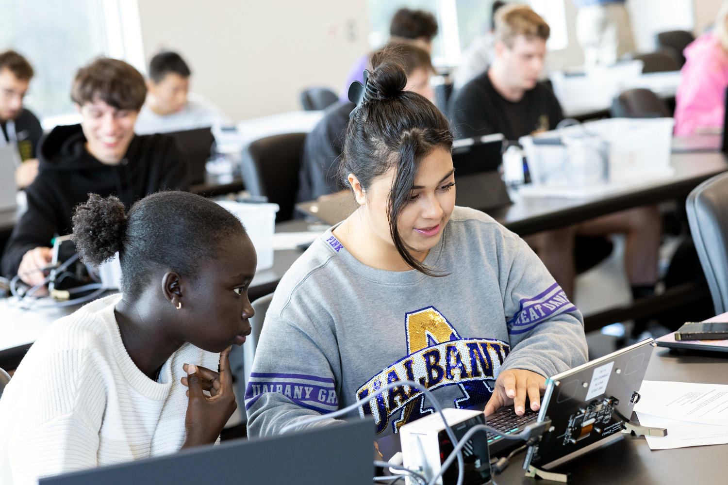 Two students working on electronic devices in a Concepts of Artificial Intelligence class.