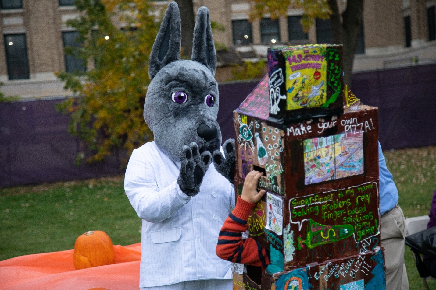 Damien the Great Dane high fives a child wearing a Halloween costume during a holiday event on campus.