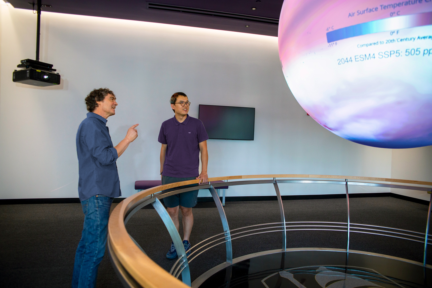 Two researchers analyzing data while standing next to a large globe in the UAlbany ETEC Science on a Sphere room.