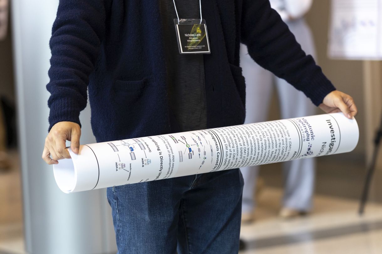 A person wearing a dark blue sweater and jeans rolls up a research poster at the end of the event.