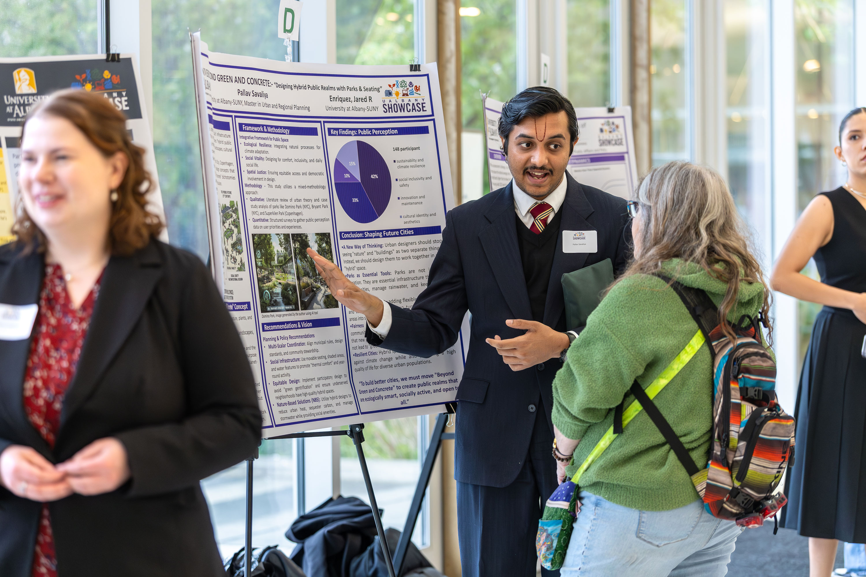 A student presenter gestures toward his research poster while speaking with a Showcase attendee.
