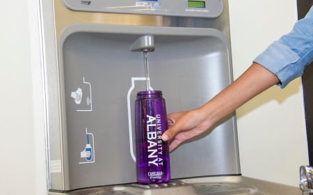 An arm and hand are seen refilling a water bottle printed with University at Albany