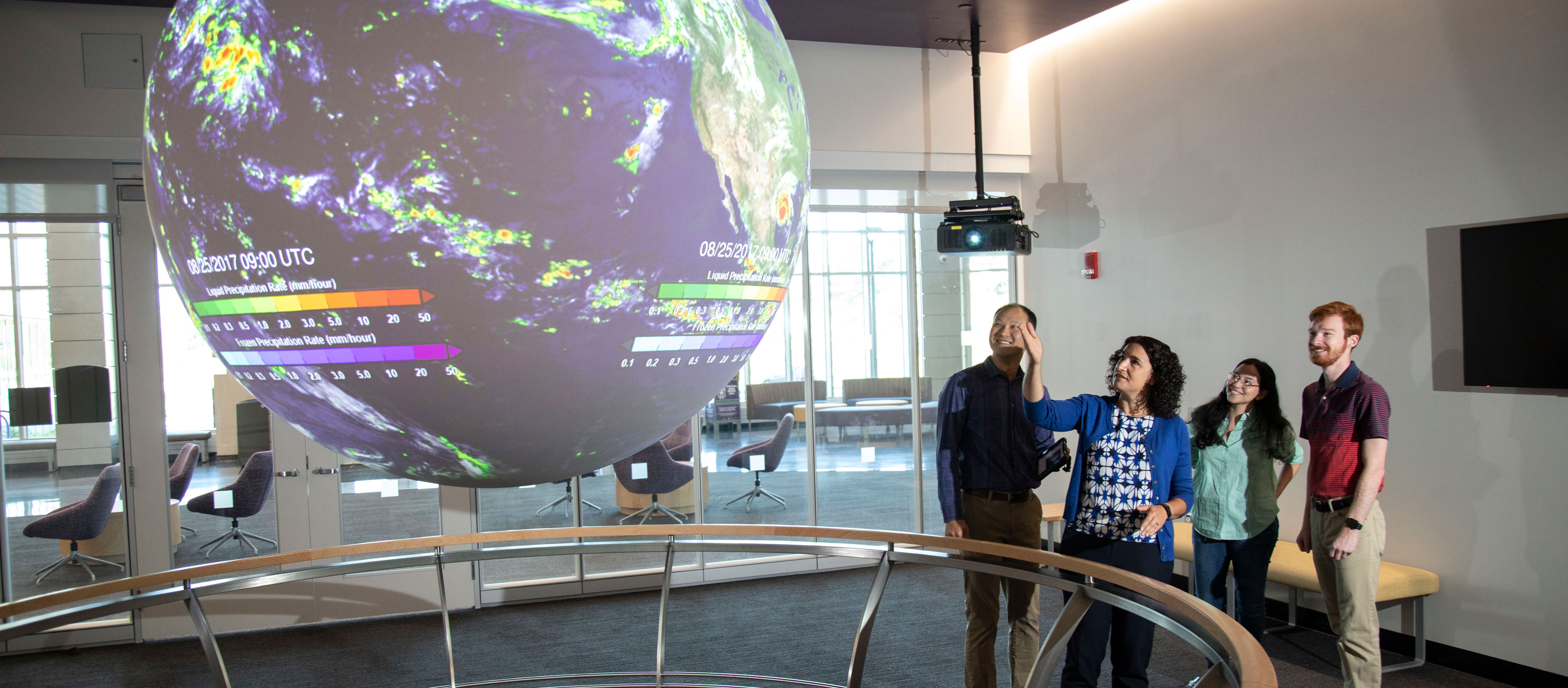 One person points at a holographic globe inside ETEC while three others look on.