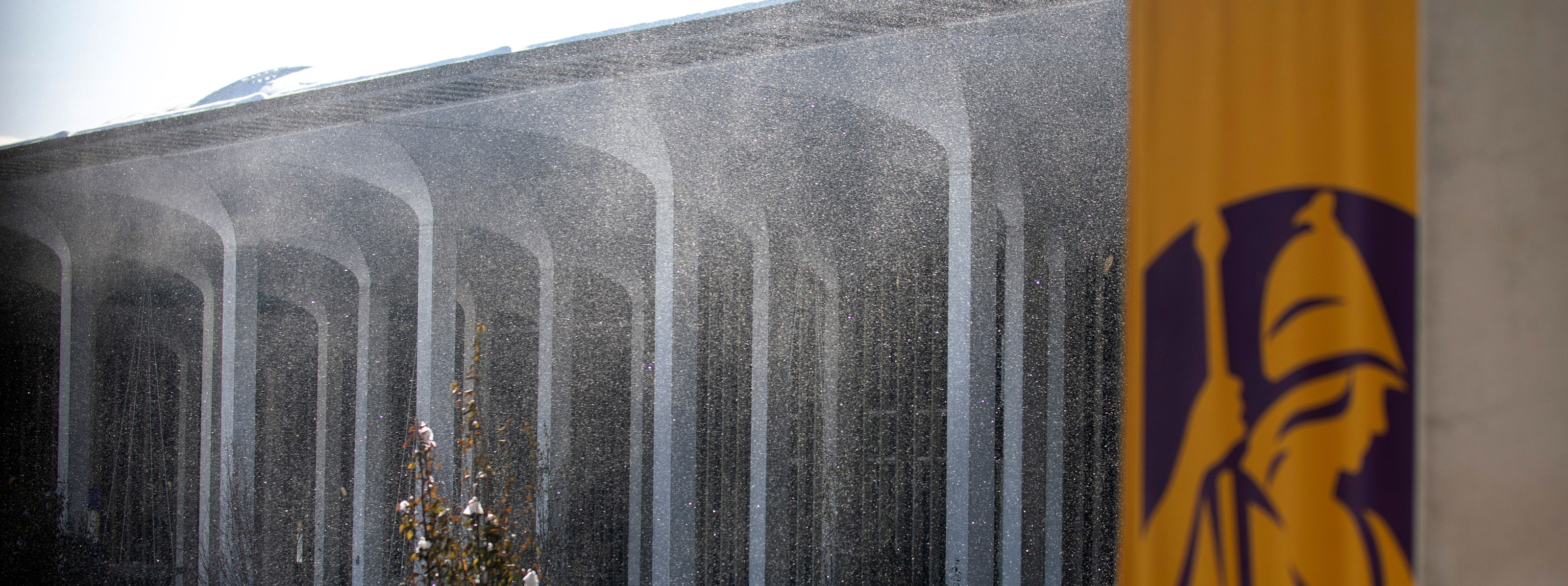 A snow squall envelopes an academic building, with a purple and gold UAlbany banner in the foreground.
