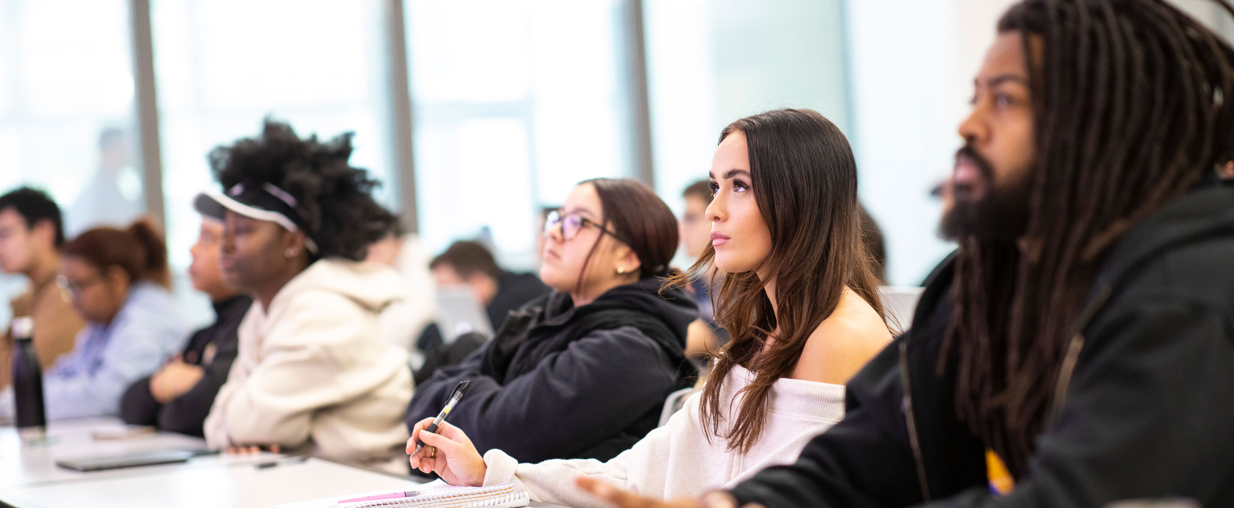 A classroom of students sit and listen to an off-camera instructor.