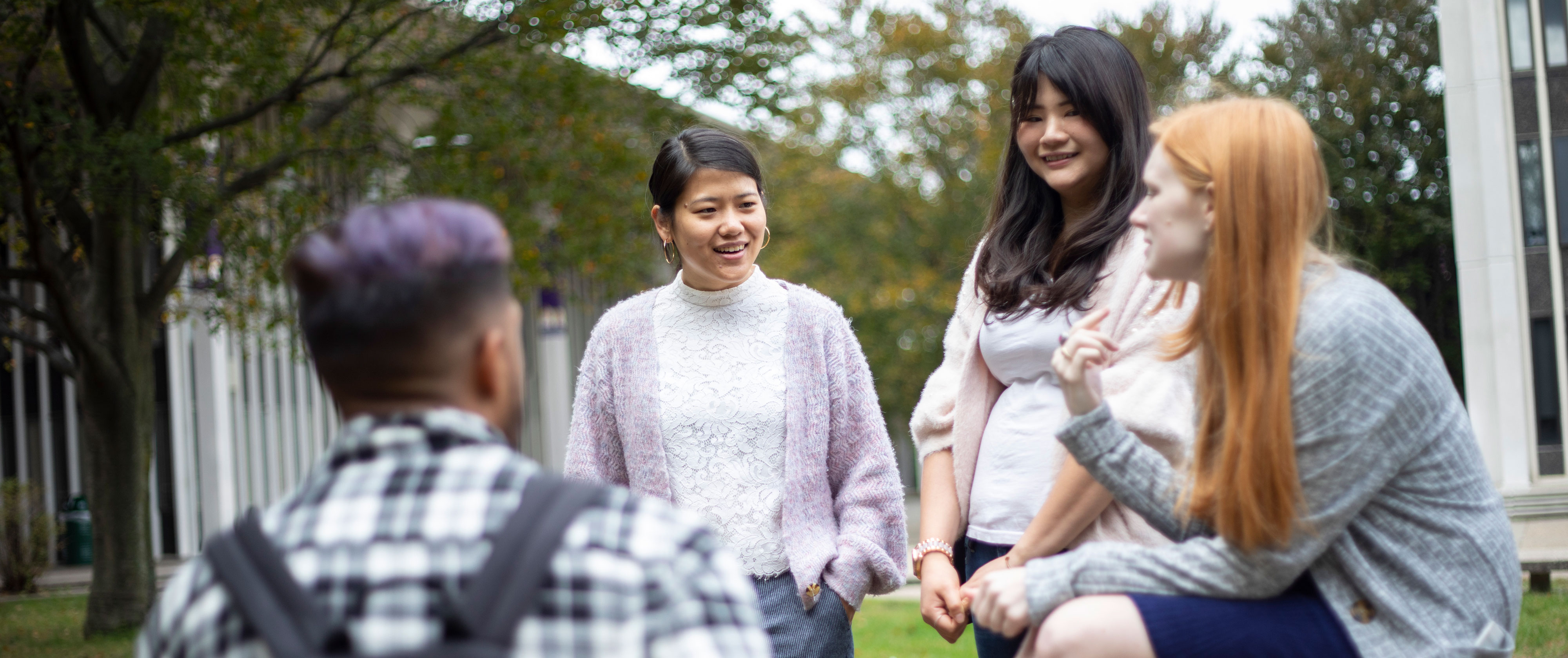 Four smile students gather outside on the UAlbany Uptown Campus on a spring day to talk.