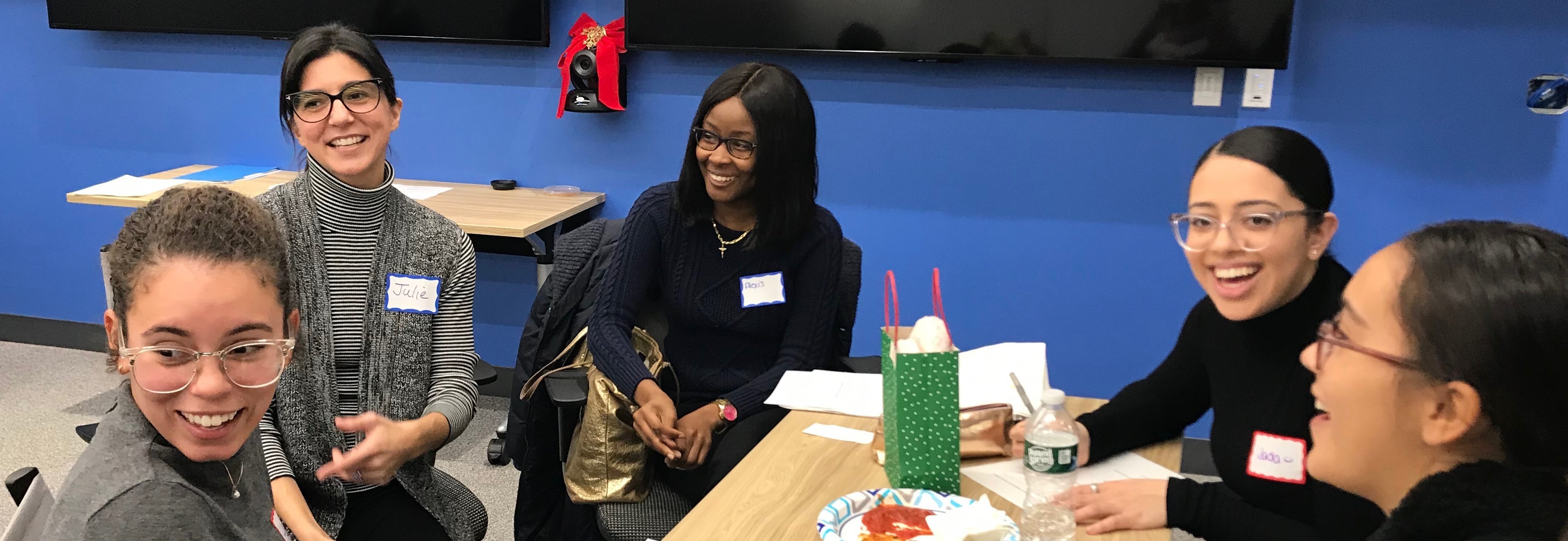 4 students and 1 faculty member sitting around conference table chatting and laughing