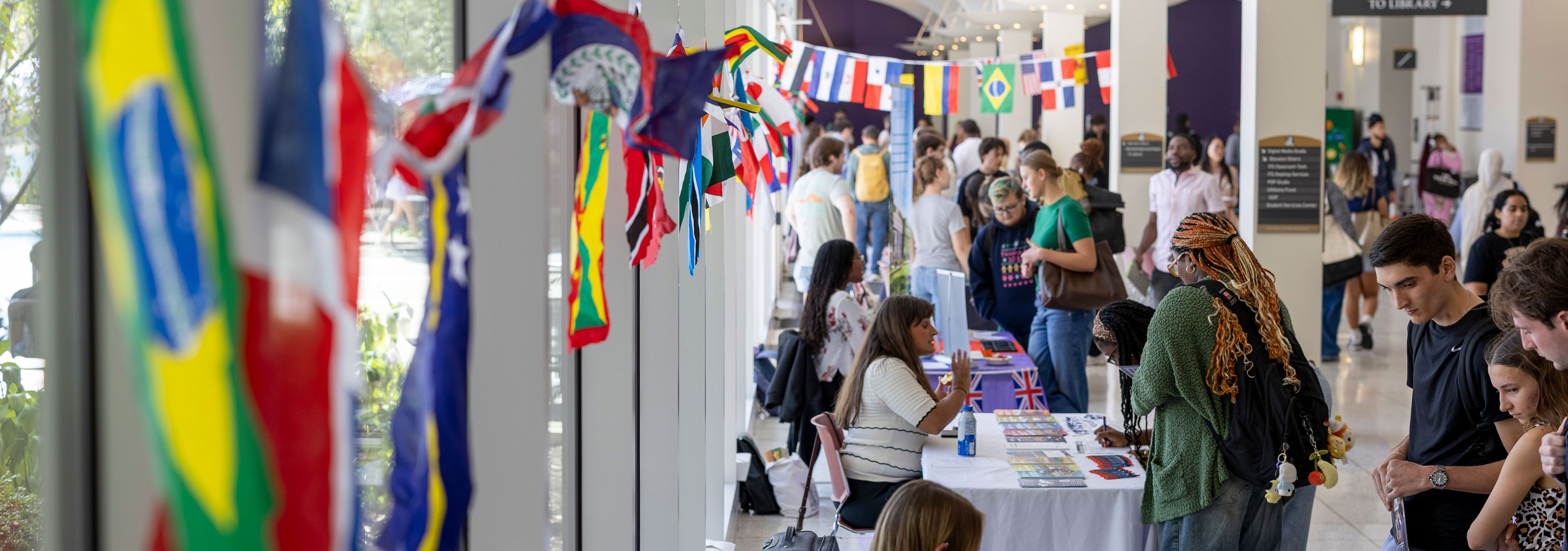 Students attend a study abroad fair at UAlbany. Flags from around the world adorn the area surrounding tables where international education professionals speak with students.