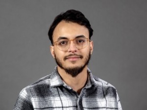 A man in glasses and a plaid shirt against a gray backdrop