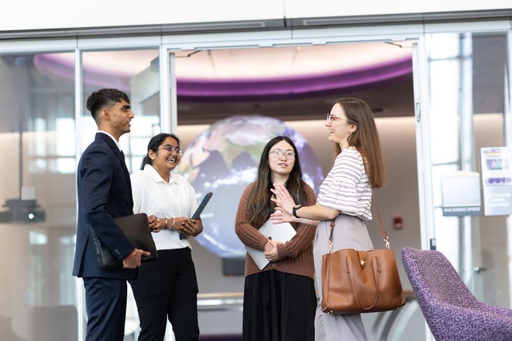 Four graduate students smile and laugh as they talk inside UAlbany's ETEC building.