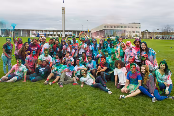 A group of students pose, smiling for a photo after participating in Holi. They are covered in colorful powders.
