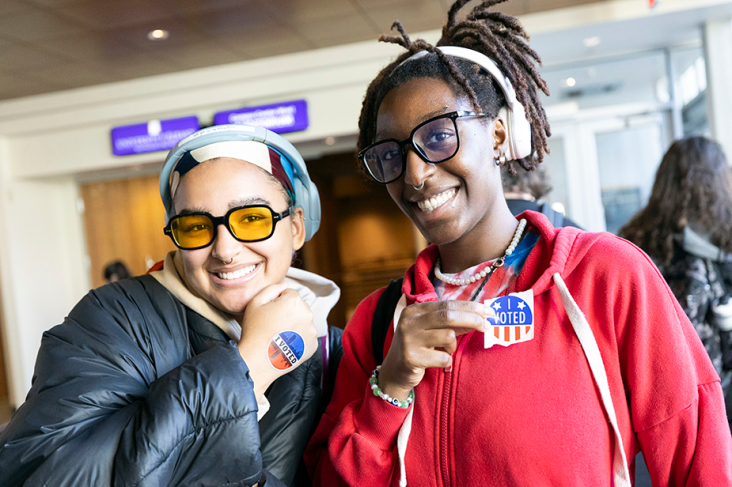 Two students smilke, showing off some stickers that read "I Voted."