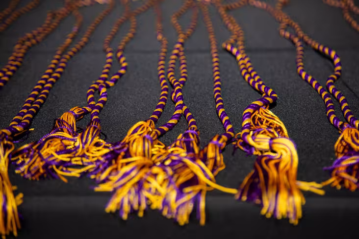 A group of purple and gold stoles lay on a table with a black tablecloth under them.