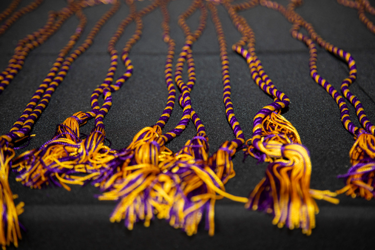 A group of purple and gold stoles lay on a table with a black tablecloth under them.