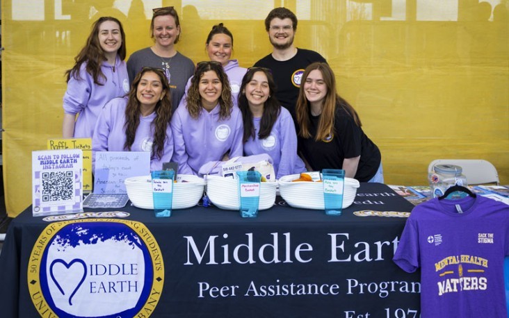 Students gather at a table with a Middle Earth Peer Assistance Program banner draped over it.