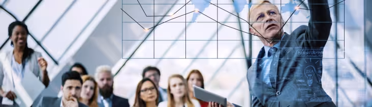 Business instructor pointing at a graph with a group of young professionals.