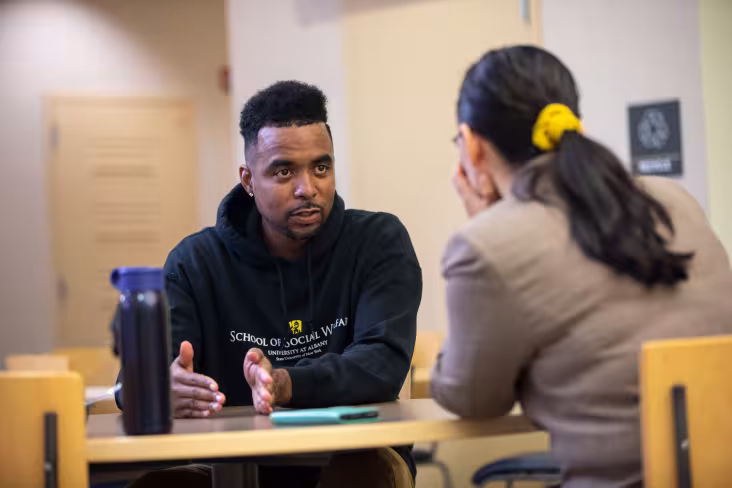 A student gestures while speaking with an advisor seated across the table.