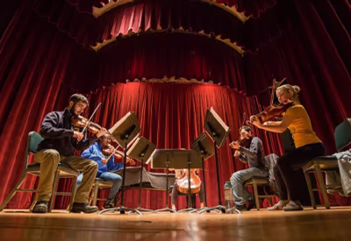 Students perform onstage with instruments and music stands at the UAlbany Performing Arts Center.
