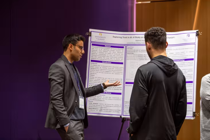 A researcher gestures to a poster while discussing findings with a conference attendee.