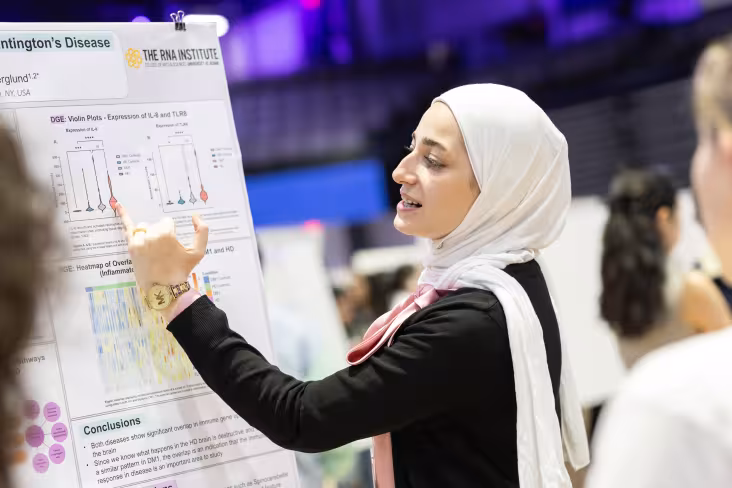 A student points with a pinky finger at a portion of her research poster while presenting at UAlbany Showcase.