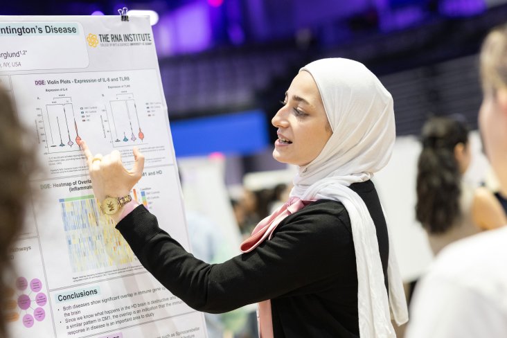 A student points with a pinky finger at a portion of her research poster while presenting at UAlbany Showcase.