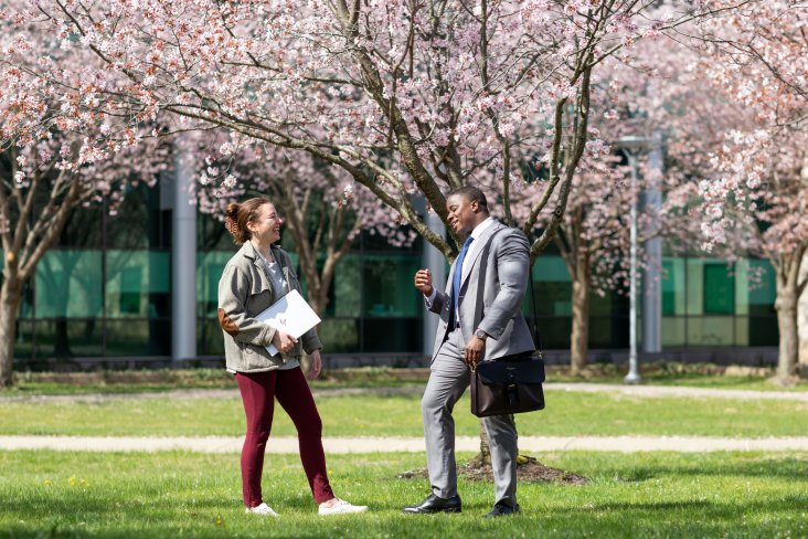 Two graduate students laugh as they stand and talk on green patch of grass on UAlbany's Uptown Campus.