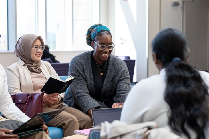 Graduate students smile and laugh while they sit inside a UAlbany academic building.