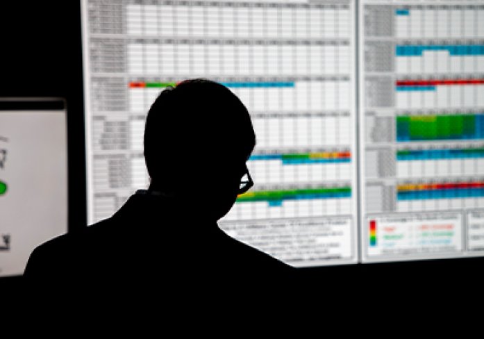 A man is silhouetted against a wall of monitors displaying weather data.