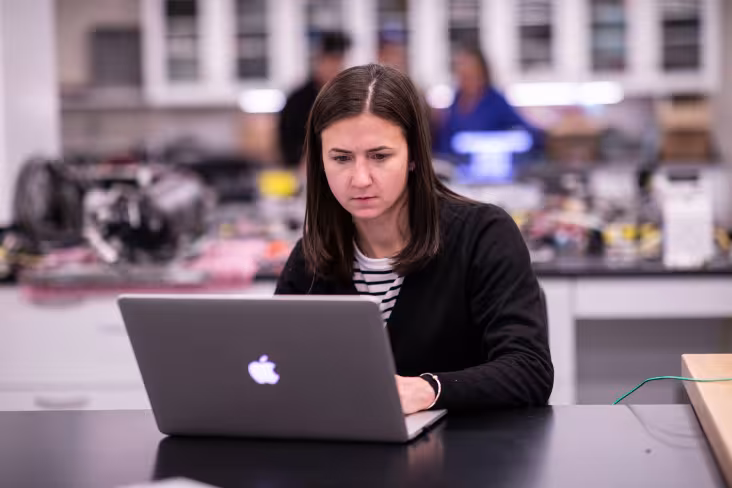 A woman sits at a desk inside a communal office and works on a laptop computer.