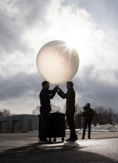 Two people hold onto a weather balloon as they prepare to release it outdoors.