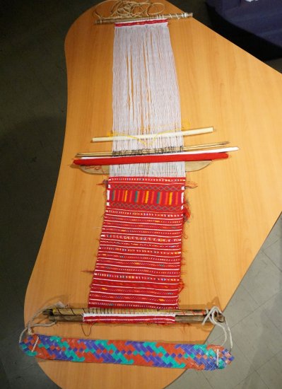 A half finished red weaving on a backstrap loom.