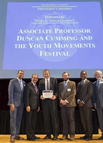 Music Associate Professor Duncan Cumming won a 2018 Exemplary Public Engagement Award. Seen here posing with five other men on stage in front of screen.