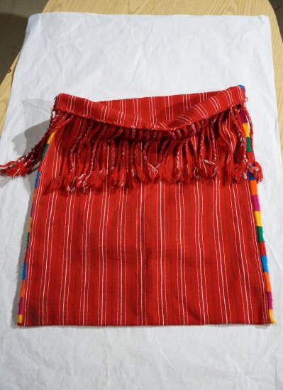 A man's red bag with white stripes, red rope fringe and colorful stitching.